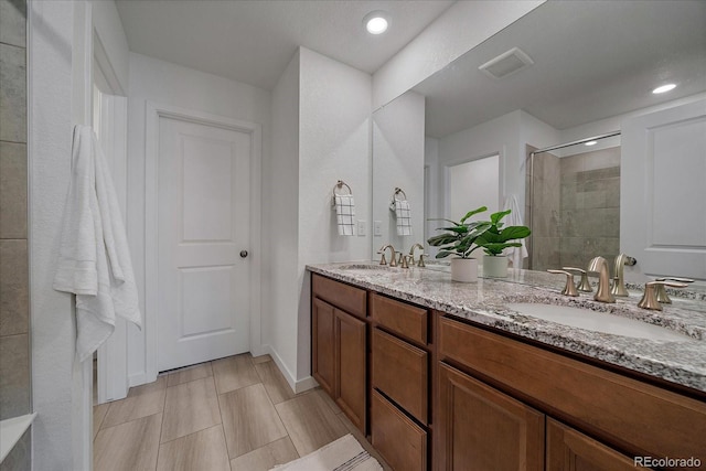 bathroom featuring double vanity, visible vents, a sink, and tiled shower