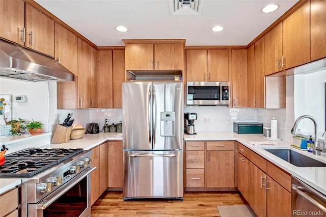 kitchen with light wood finished floors, stainless steel appliances, visible vents, a sink, and under cabinet range hood