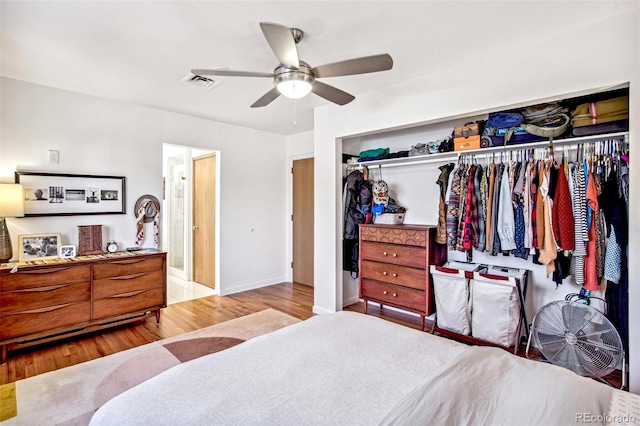 bedroom with ceiling fan, wood finished floors, visible vents, baseboards, and a closet