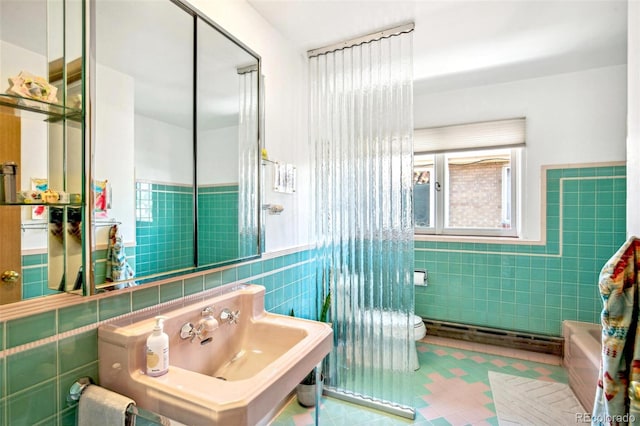 bathroom with toilet, a baseboard heating unit, a wainscoted wall, a sink, and tile walls