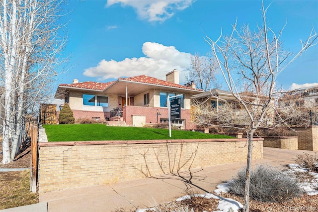 view of front of property featuring brick siding, a chimney, a tiled roof, fence, and a front yard