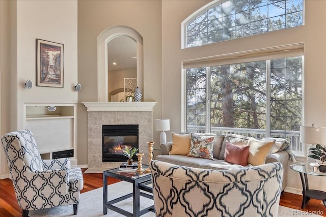 living area featuring a tiled fireplace, wood finished floors, a towering ceiling, and baseboards