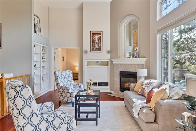 living area featuring wood finished floors, a high ceiling, a tile fireplace, and built in shelves