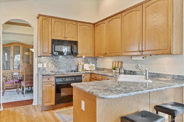 kitchen featuring light wood finished floors, a breakfast bar area, a peninsula, black appliances, and a sink