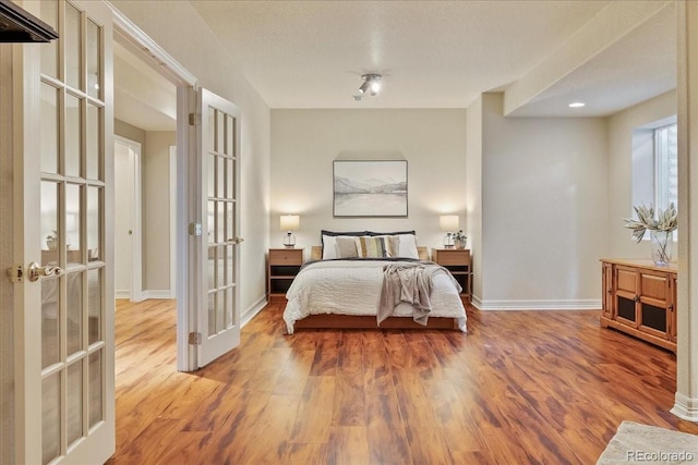 bedroom featuring baseboards, wood finished floors, and french doors