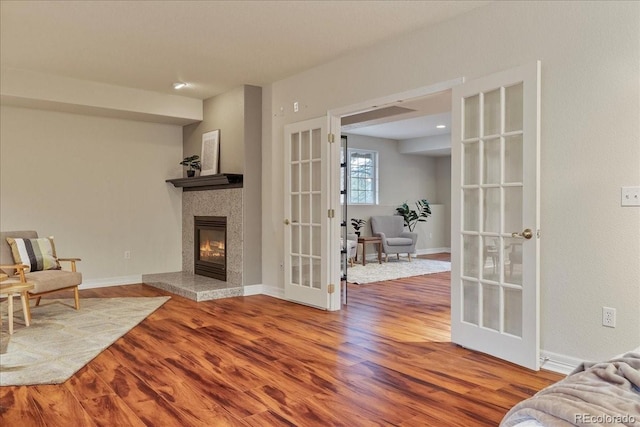 sitting room with french doors, a tiled fireplace, wood finished floors, and baseboards