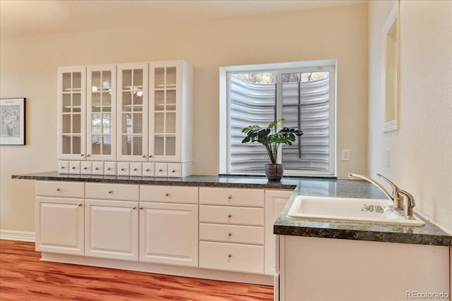 kitchen with glass insert cabinets, dark countertops, white cabinets, and a sink