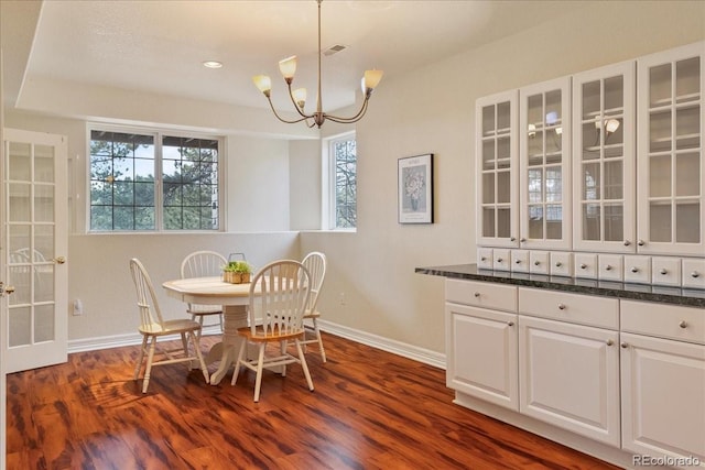 dining space with dark wood-type flooring, an inviting chandelier, and baseboards