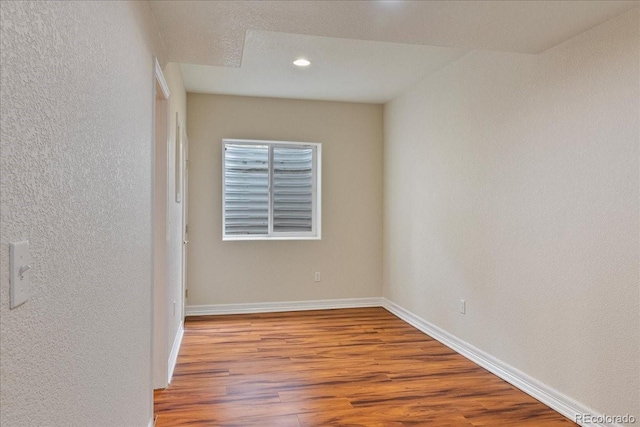 spare room with a textured wall, wood finished floors, and baseboards