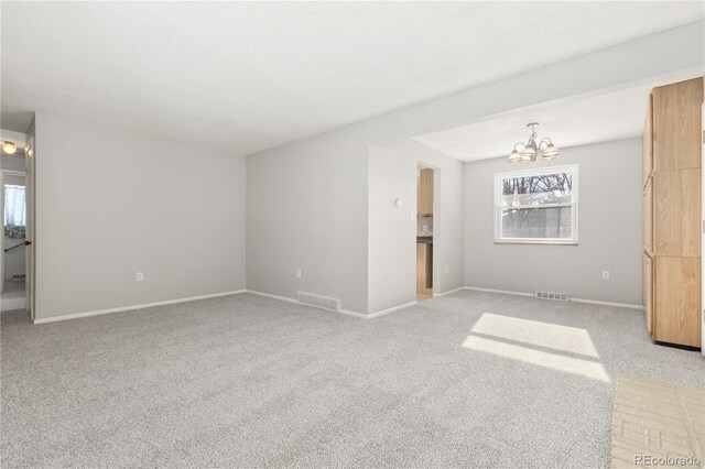 empty room featuring light colored carpet and a notable chandelier