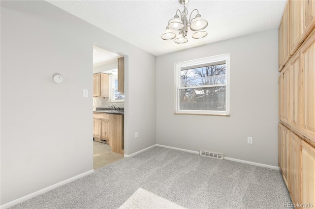 spare room with sink, light carpet, and an inviting chandelier