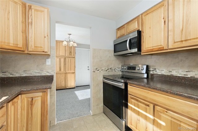 kitchen featuring decorative backsplash, light brown cabinetry, dark stone counters, stainless steel appliances, and a chandelier