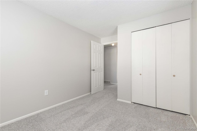 unfurnished bedroom featuring light colored carpet, a textured ceiling, and a closet