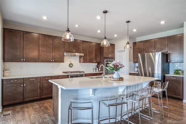 kitchen with under cabinet range hood, stainless steel appliances, dark wood-style flooring, and a kitchen bar