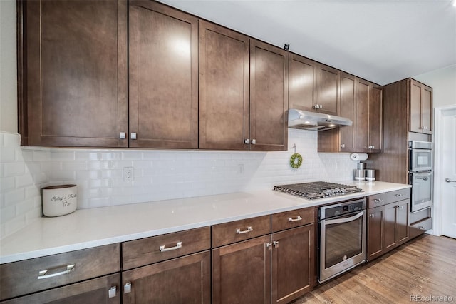 kitchen featuring stainless steel gas cooktop, dark brown cabinetry, light countertops, under cabinet range hood, and light wood finished floors