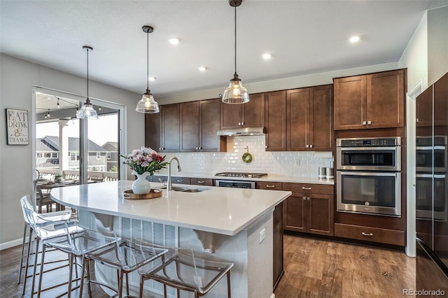 kitchen with a sink, light countertops, backsplash, under cabinet range hood, and dark wood-style floors