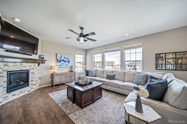 living room with wood finished floors, baseboards, a stone fireplace, ceiling fan, and recessed lighting