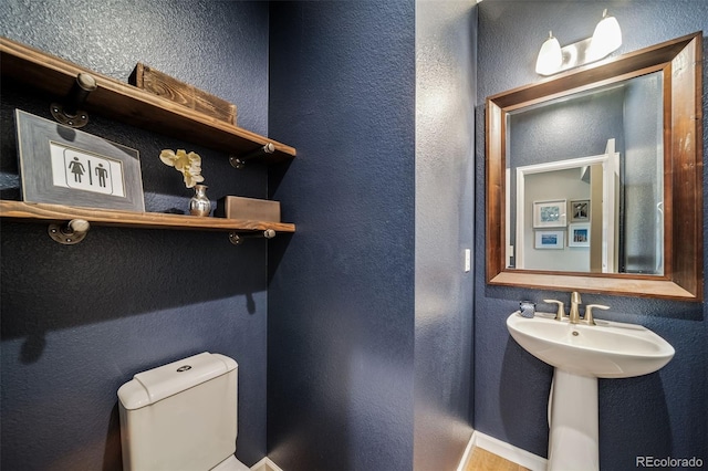half bath with a sink, a textured wall, and toilet