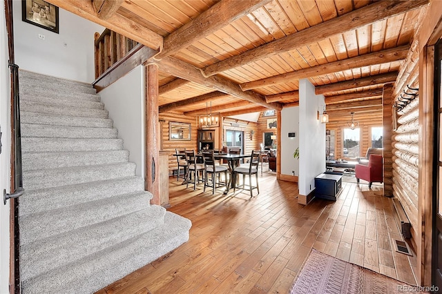 stairs with wood ceiling, hardwood / wood-style flooring, an inviting chandelier, log walls, and beamed ceiling