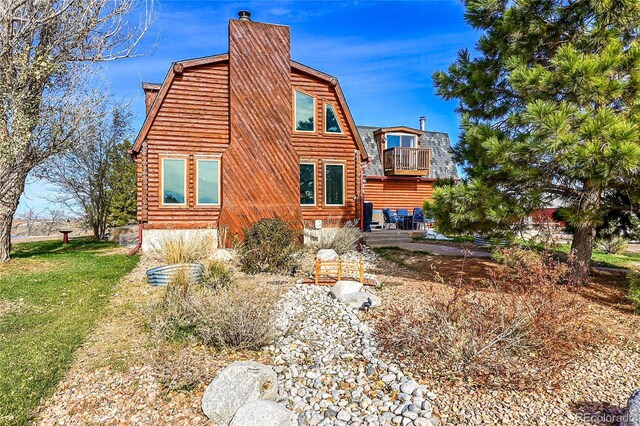 48155 E 56th Ave, Bennett, CO 80102 - view of side of property featuring a chimney, a gambrel roof, a balcony, log exterior, and a lawn
