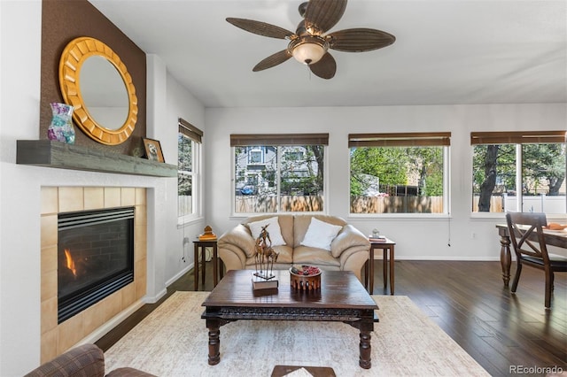 living area with a tiled fireplace, baseboards, wood-type flooring, and a ceiling fan