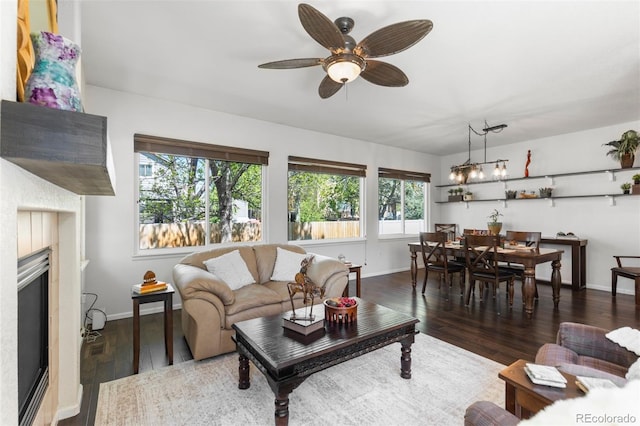 living room with baseboards, a glass covered fireplace, ceiling fan, and wood finished floors