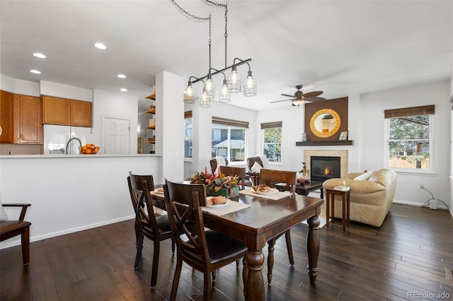 dining space with ceiling fan, a tiled fireplace, recessed lighting, a healthy amount of sunlight, and dark wood-style floors