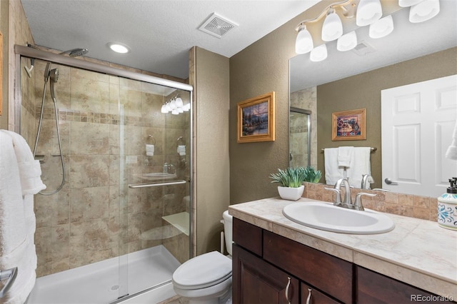 bathroom with vanity, a stall shower, toilet, and visible vents