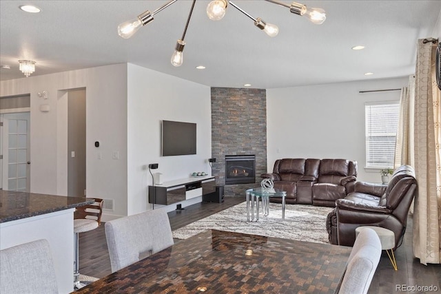 living room with dark wood finished floors, a stone fireplace, recessed lighting, and visible vents