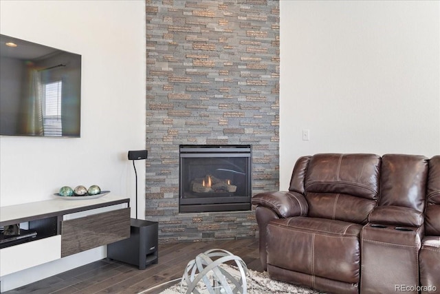 living area featuring a stone fireplace and dark wood-style flooring