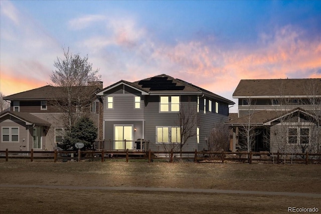 rear view of house with solar panels, a wooden deck, a fenced backyard, and a chimney