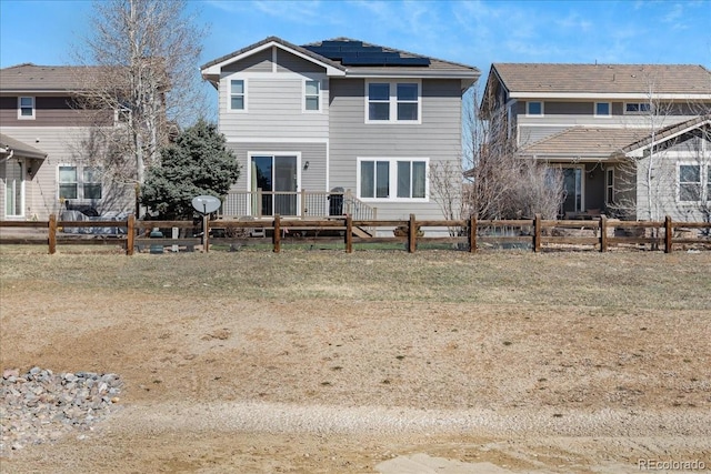 rear view of house featuring roof mounted solar panels and fence private yard