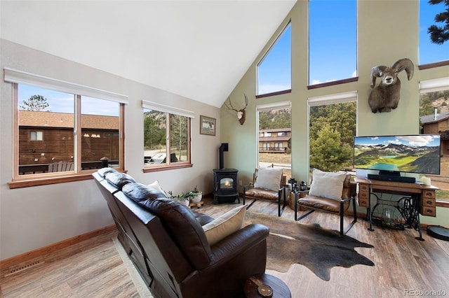 living room featuring high vaulted ceiling, a wood stove, plenty of natural light, and wood finished floors