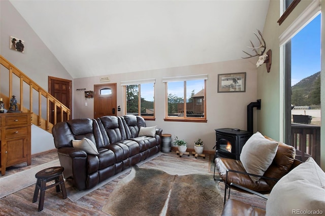 living area featuring a wood stove, plenty of natural light, wood finished floors, stairs, and high vaulted ceiling