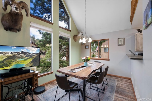 dining space with baseboards, a chandelier, high vaulted ceiling, and wood finished floors