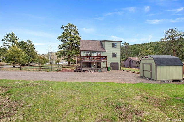 rear view of house featuring a deck, an outdoor structure, a garage, a shed, and roof with shingles
