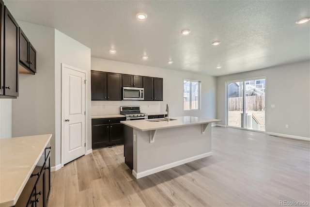 kitchen featuring a textured ceiling, light hardwood / wood-style flooring, a kitchen island with sink, stainless steel appliances, and sink