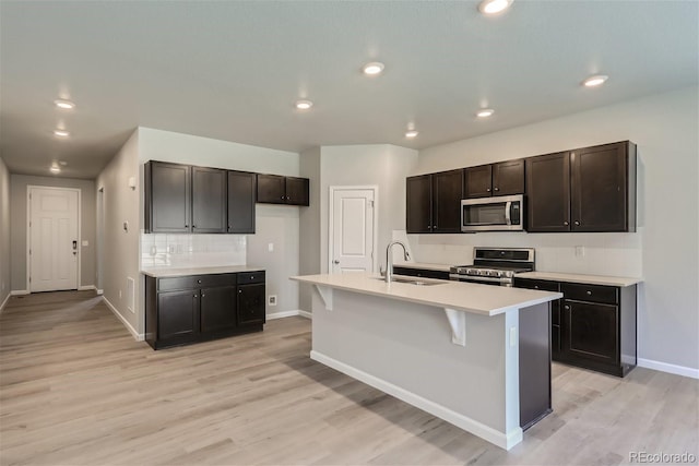 kitchen with a kitchen island with sink, tasteful backsplash, sink, appliances with stainless steel finishes, and light hardwood / wood-style floors