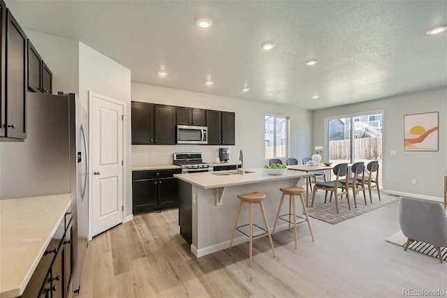 kitchen with light wood-type flooring, a textured ceiling, stainless steel appliances, and a center island with sink