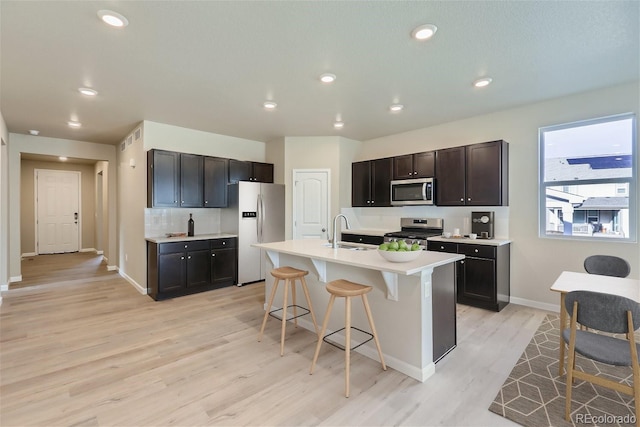 kitchen with light wood-type flooring, appliances with stainless steel finishes, sink, an island with sink, and a kitchen bar