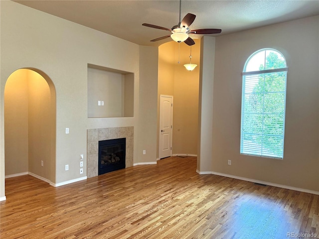 8913 Sunstone Dr, Colorado Springs, CO 80924 - unfurnished living room with wood finished floors, ceiling fan, arched walkways, baseboards, and a tiled fireplace