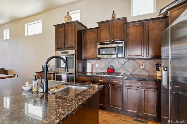 8913 Sunstone Dr, Colorado Springs, CO 80924 - kitchen with appliances with stainless steel finishes, tasteful backsplash, dark stone counters, light wood-style flooring, and dark brown cabinetry