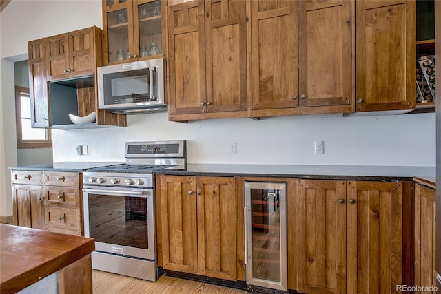 kitchen with dark countertops, wine cooler, glass insert cabinets, brown cabinets, and stainless steel appliances