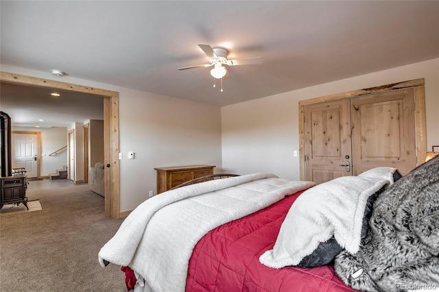 carpeted bedroom with a wood stove, ceiling fan, and baseboards