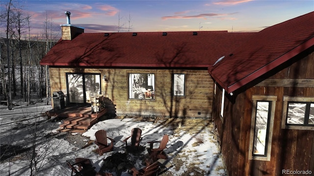 snow covered back of property featuring a chimney