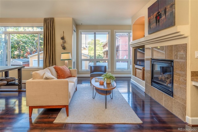 living room featuring a tiled fireplace, a healthy amount of sunlight, and dark wood-type flooring