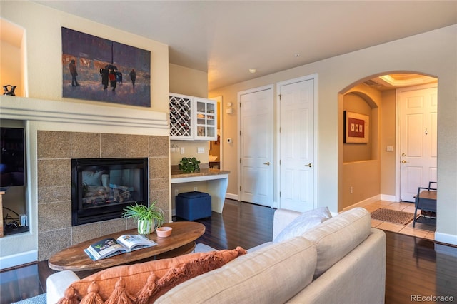 living room with a tiled fireplace, wood finished floors, arched walkways, and baseboards