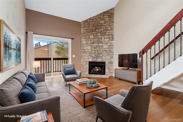 living room featuring high vaulted ceiling, light hardwood / wood-style floors, and a stone fireplace