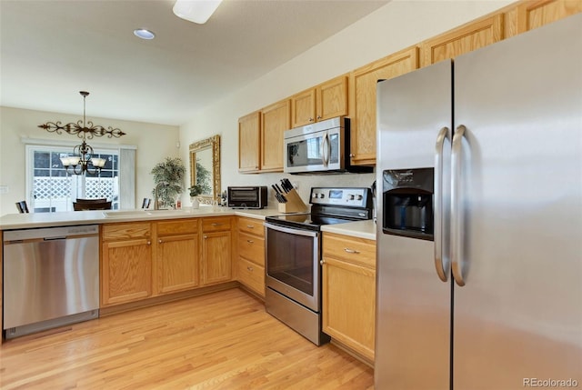 kitchen featuring a sink, light countertops, appliances with stainless steel finishes, a chandelier, and light wood-style floors
