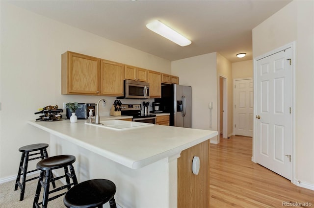 kitchen with a sink, light countertops, a peninsula, stainless steel appliances, and a breakfast bar area